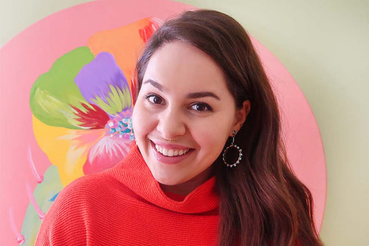 Photo of the artist in a red sweater in front of a colorful flower painting